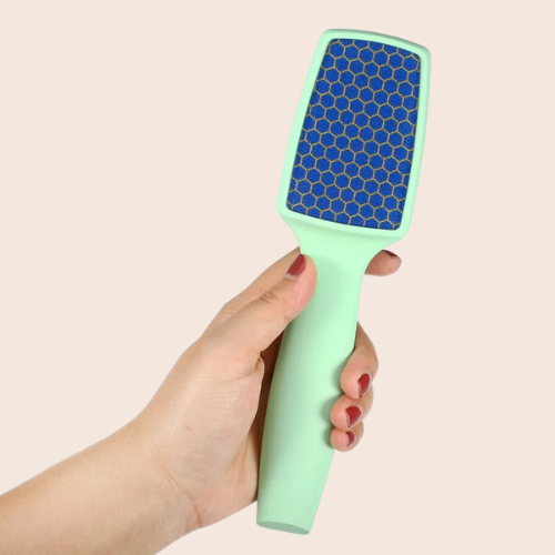Hand holding a mint-green nano-glass foot file with fine abrasive surface on a light background.